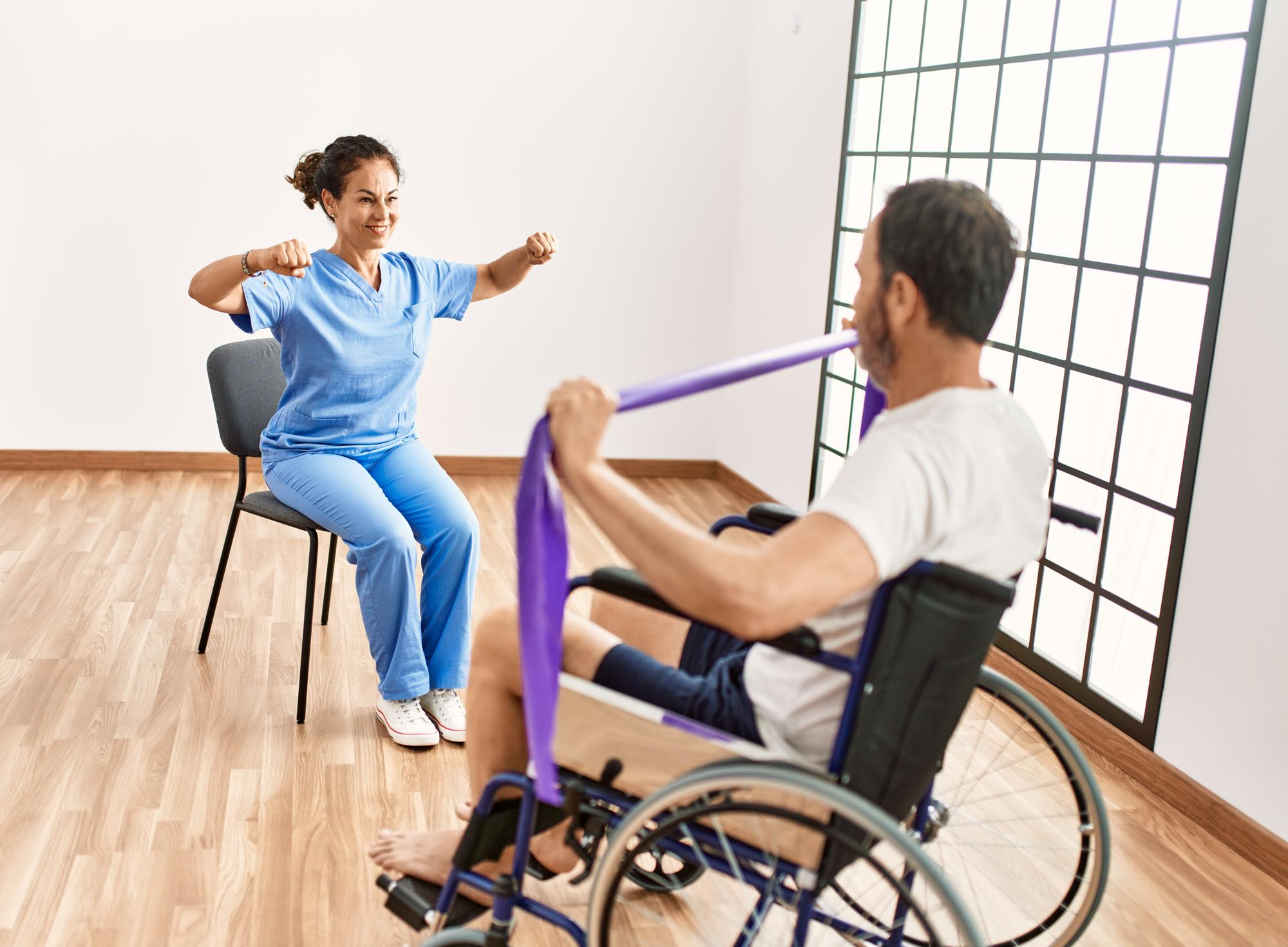 Middle age man and woman having rehab session using elastic band sitting on wheelchair at physiotherapy clinic