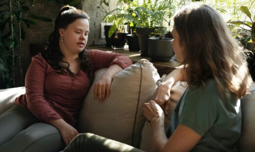 A female NDIS support coordinator from SafeLane Healthcare discusses plans with her participant, a young lady with disabilities. Both are engaged in conversation, with supportive materials on the hand